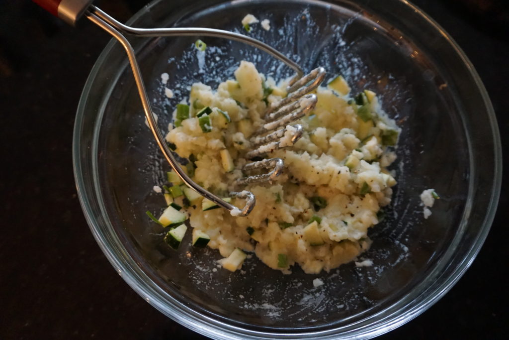 Potato filling ingredients being mashed together in a clear bowl.