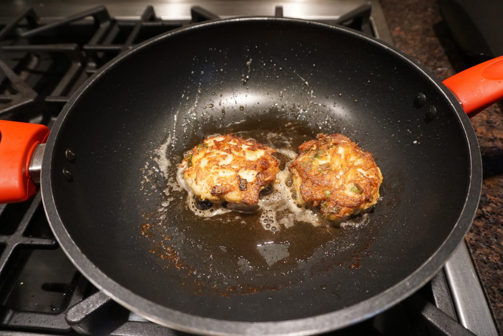 Frying FODMAP safe crab cakes in a large pan.