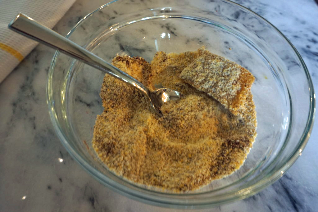 Cornmeal and seasoning in a glass bowl to be mixed with fish.