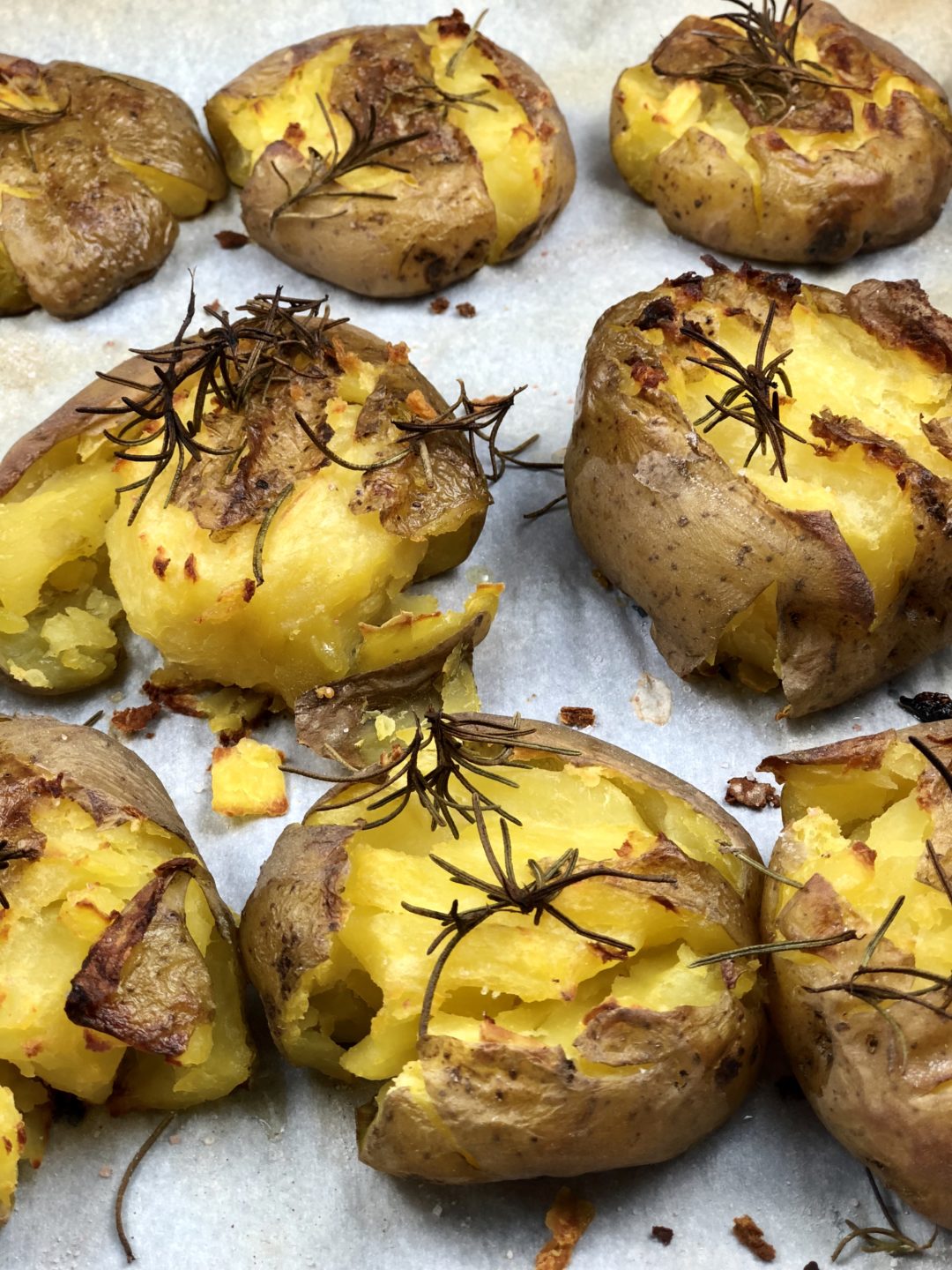 Smashed Potatoes topped with salt, rosemary and olive oil on a parchment lined baking sheet. - FODMAP smashed dish