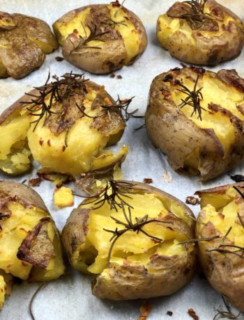 Smashed Potatoes topped with salt, rosemary and olive oil on a parchment lined baking sheet. - FODMAP smashed dish