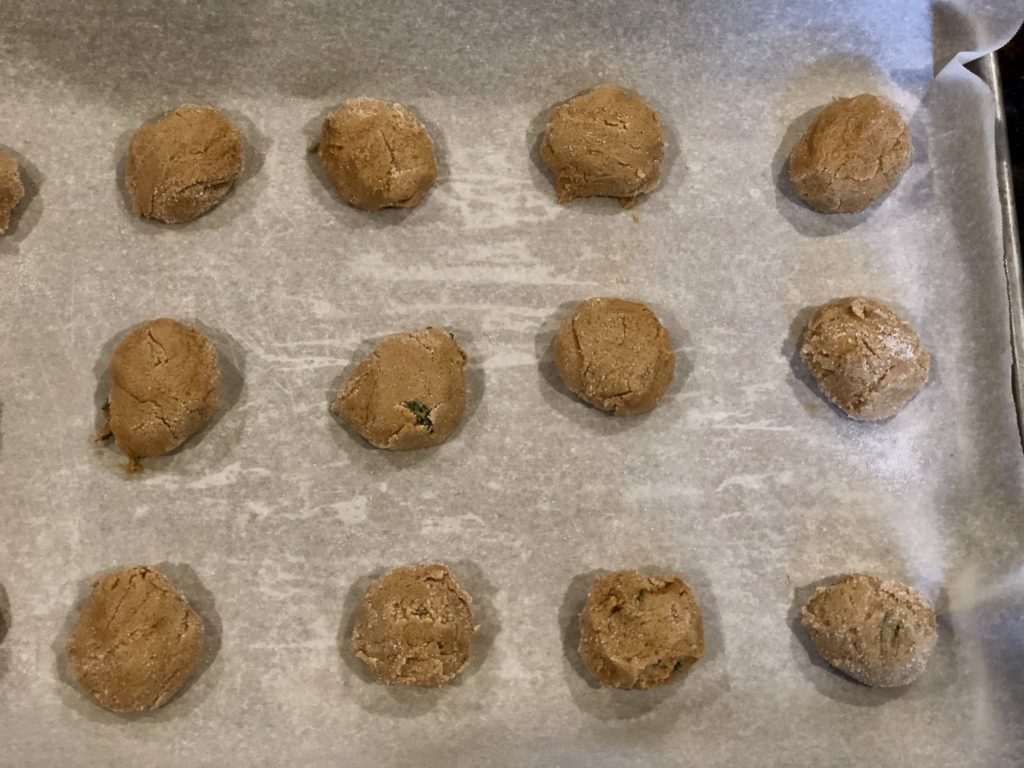 Cookies rolled in sugar and ready to be baked on a lined baking sheet.