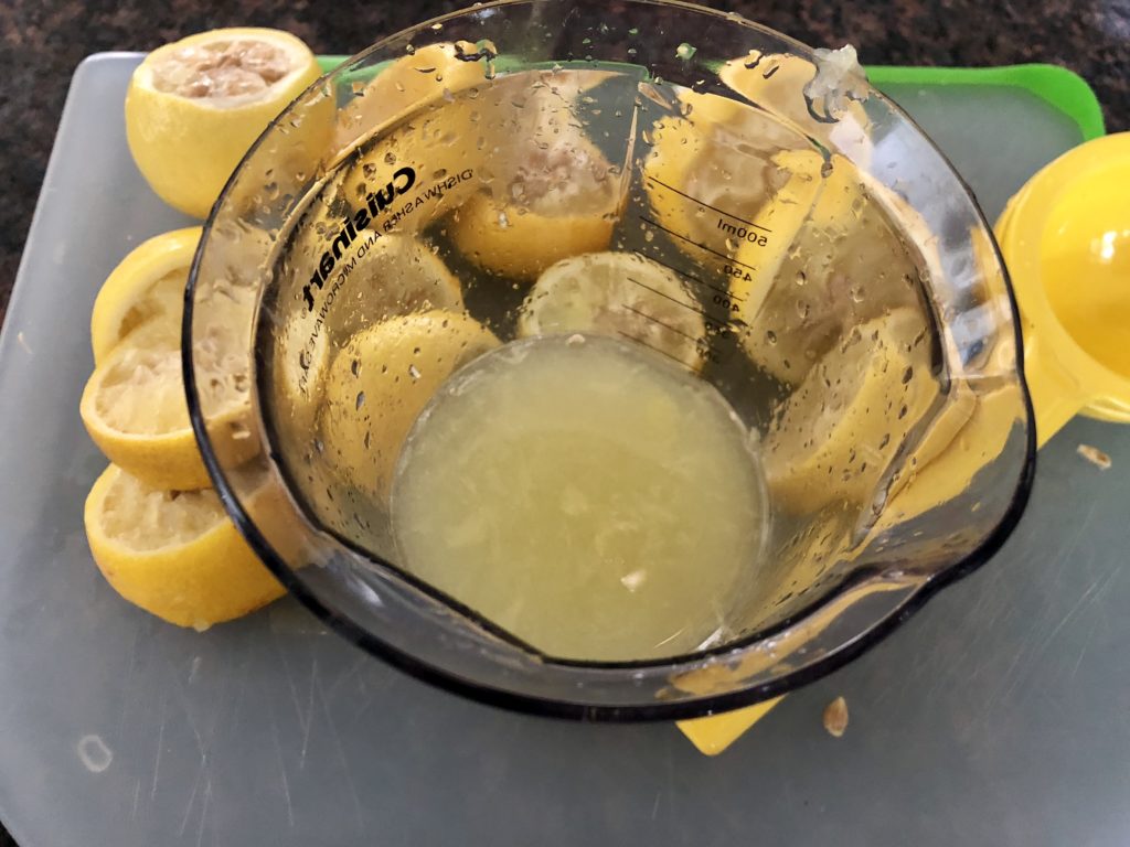 Fresh lemons being juiced into a measuring cup.