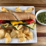 FODMAP safe grilled vegetable sandwich with chips and a side of pesto on a white plate.