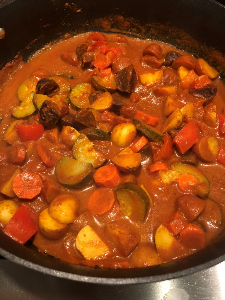 Shrimp, vegetables & curry sauce being cooked in a large pan.